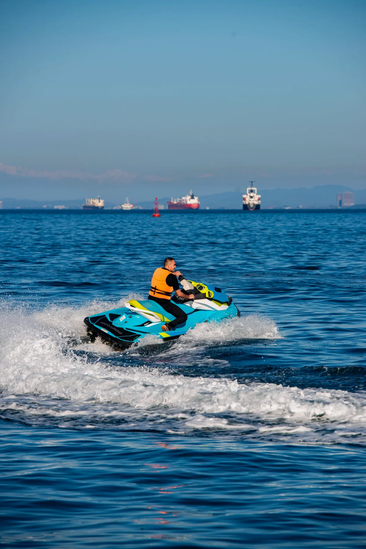 Moto de agua navegando frente a la costa, con barcos de fondo
