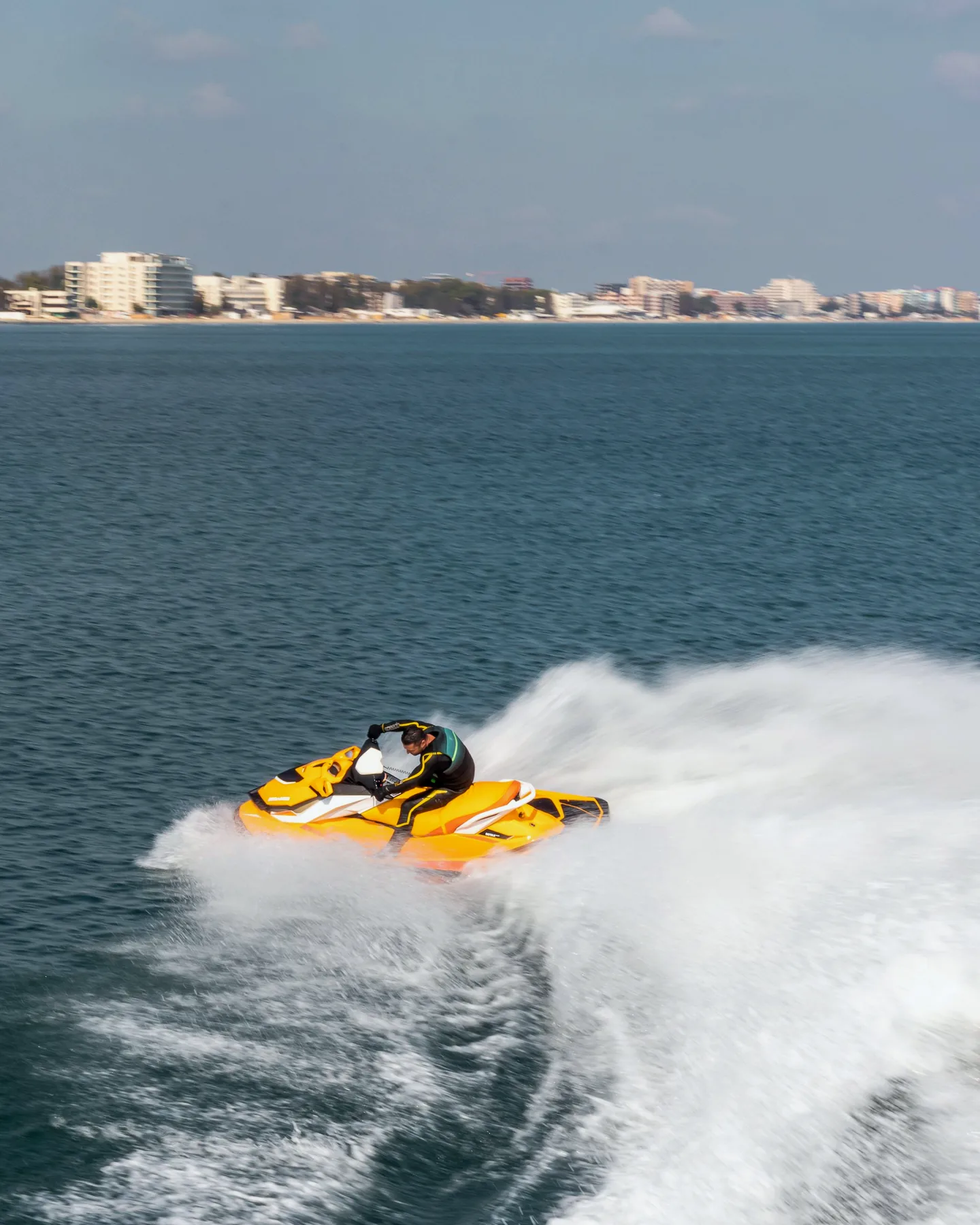 Moto de agua amarilla acelerando frente a una costa urbanizada